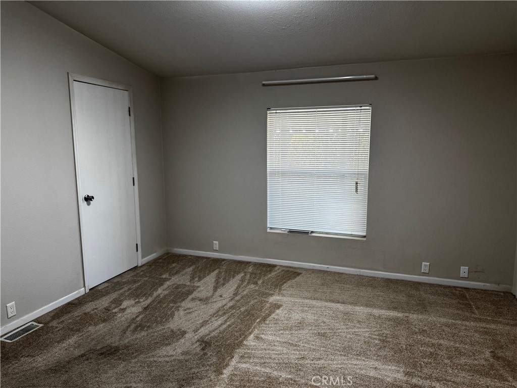 Empty bedroom with beige carpet, gray walls, and a window with closed blinds.