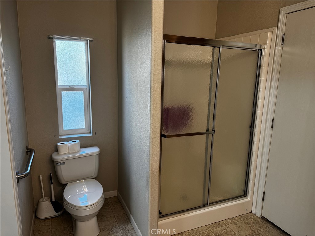 Bathroom with a toilet beneath a narrow window beside a corner shower with sliding glass doors.