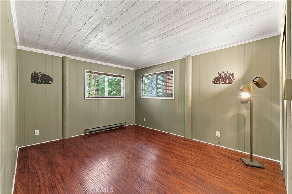 Unfurnished room with reddish-brown flooring, sage-green paneled walls, two windows, and a white plank ceiling.