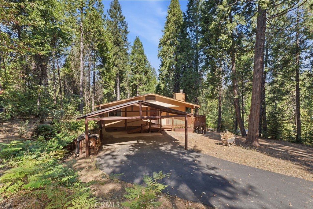 Wood-sided home with a covered carport and deck, surrounded by tall trees.