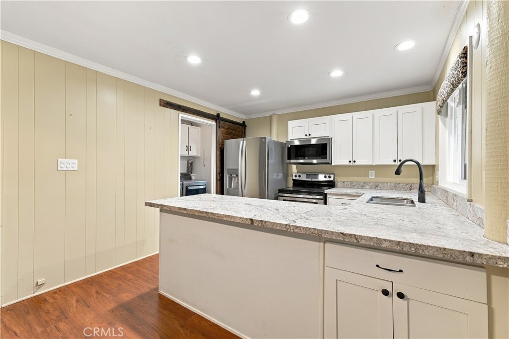 Kitchen with white cabinets, stone counters, a wide peninsula, and stainless steel appliances.