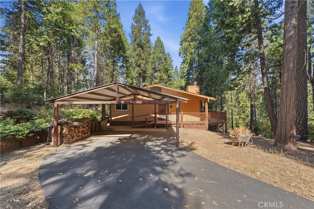 Tan home with a covered carport and wooden deck among tall trees.