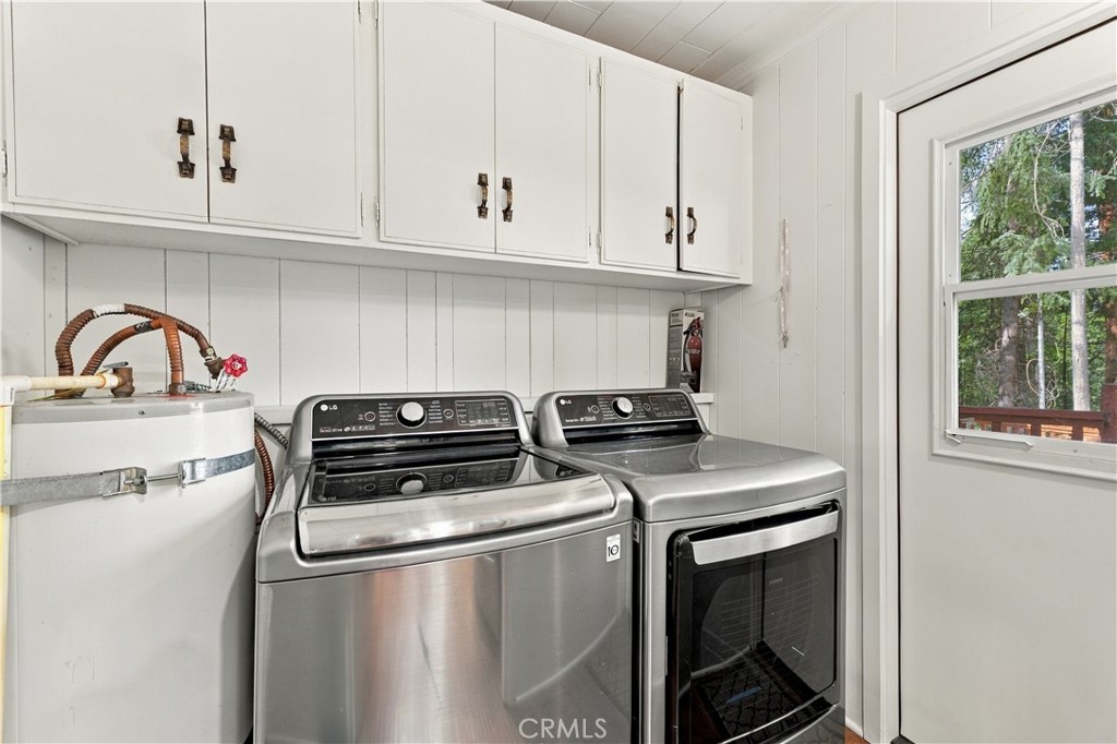 Laundry room with stainless washer and dryer, overhead cabinets, and a window overlooking trees.
