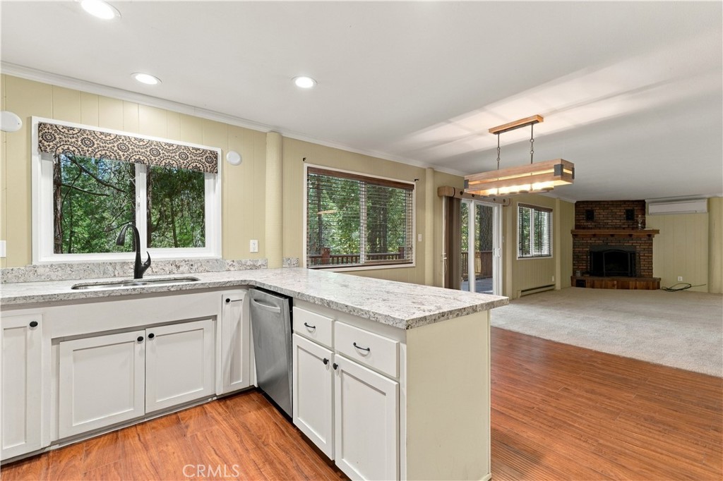 Kitchen with white cabinets and granite counters opens to a living room with a brick fireplace.
