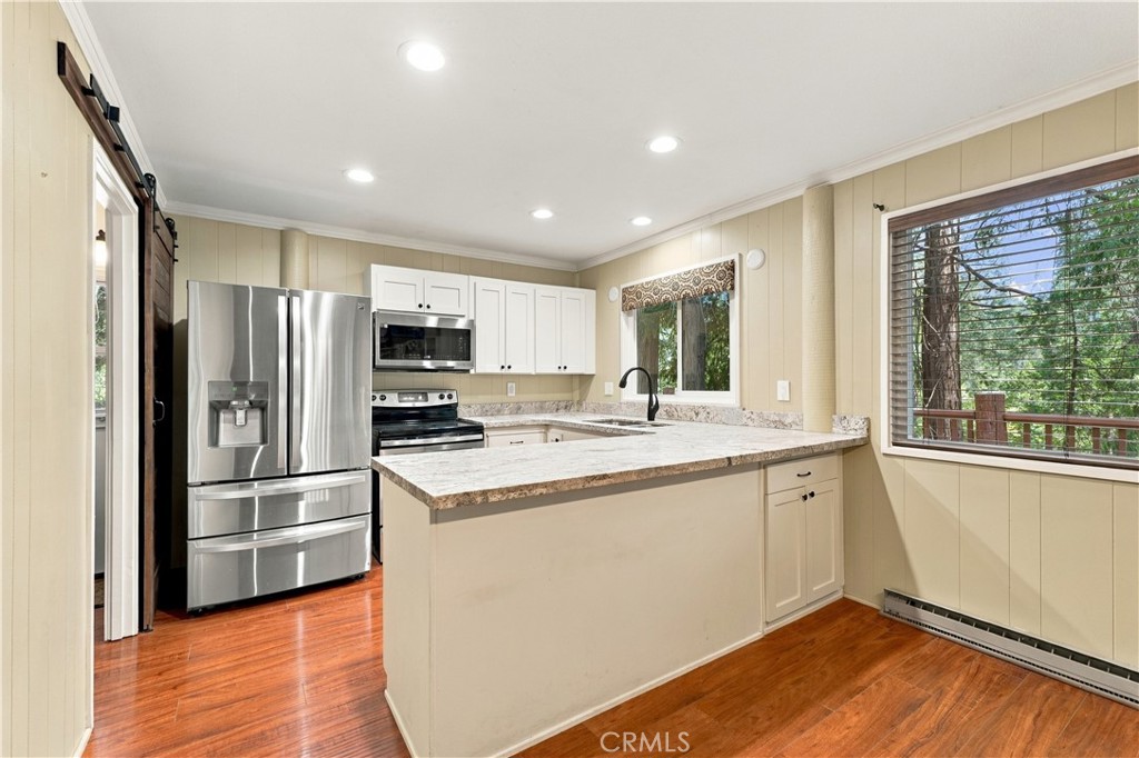 Kitchen with stainless steel appliances, a large stone-topped peninsula, and windows overlooking trees.