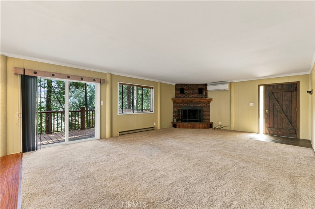 Vacant living room with a brick fireplace and sliding doors opening onto a wooded deck.