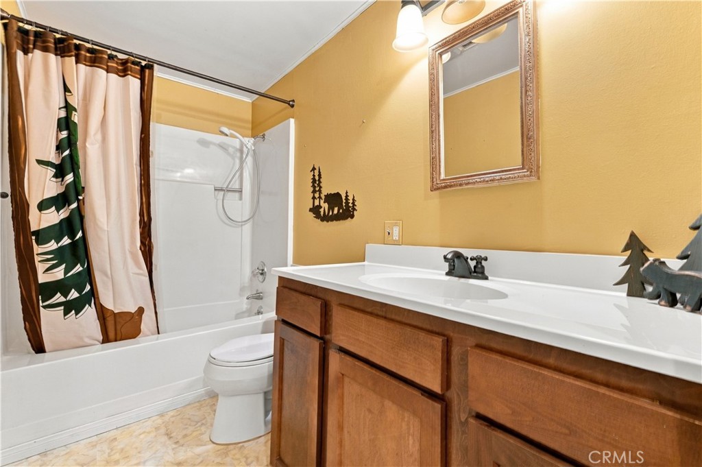 Bathroom with a wooden vanity, white tub and shower, and patterned curtain.