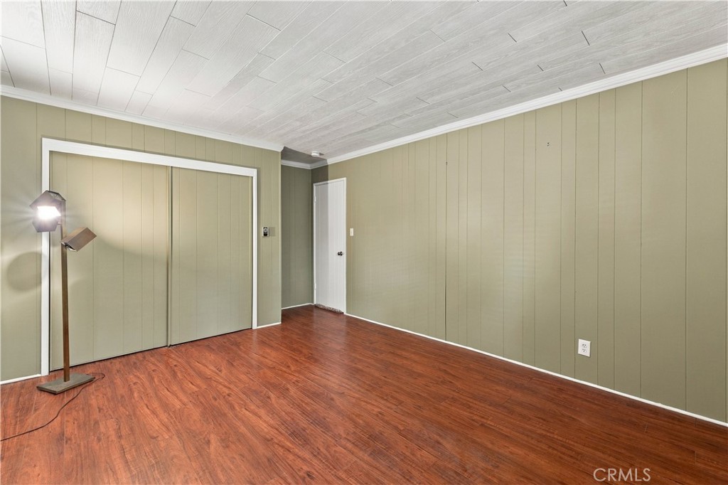 Vacant room with sliding closet doors, olive-green paneled walls, and reddish wood-look flooring.