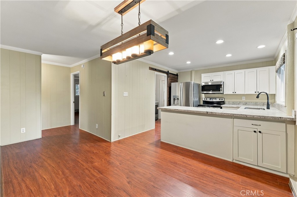 Unfurnished kitchen and dining area with white cabinets, stainless steel appliances, and reddish wood flooring.