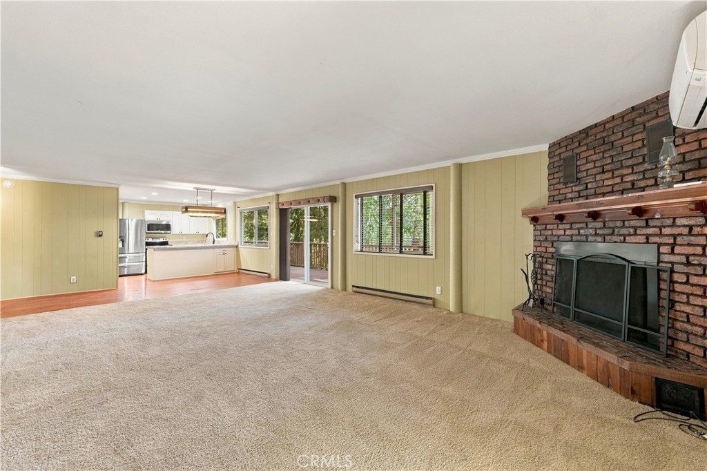 Unfurnished living room with beige carpet, brick fireplace, and an open kitchen.