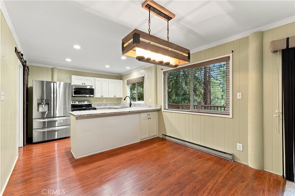 Kitchen with white cabinets, granite counters, stainless steel appliances, and a large window overlooking trees.