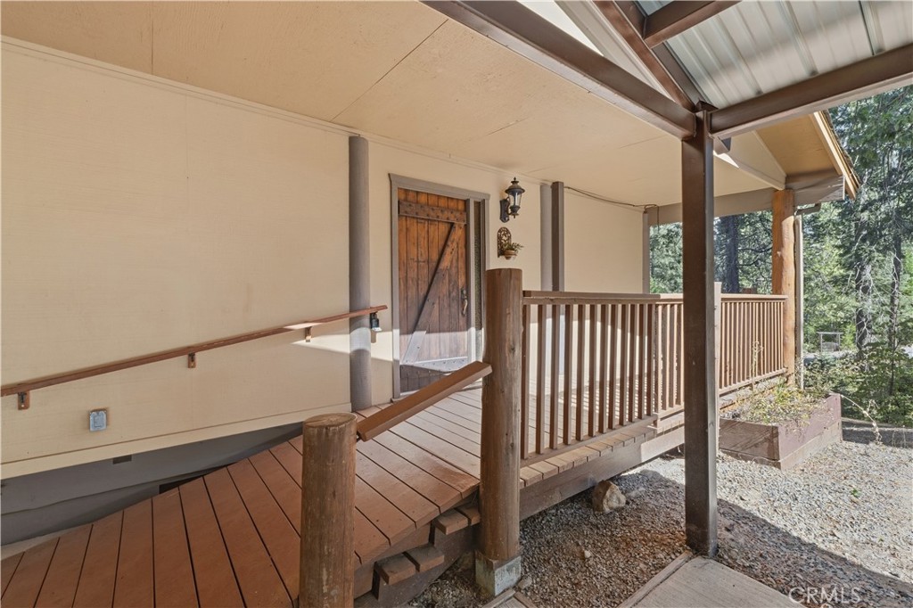 Covered wooden porch with a rustic barn-style door, ramp, and wooded surroundings.