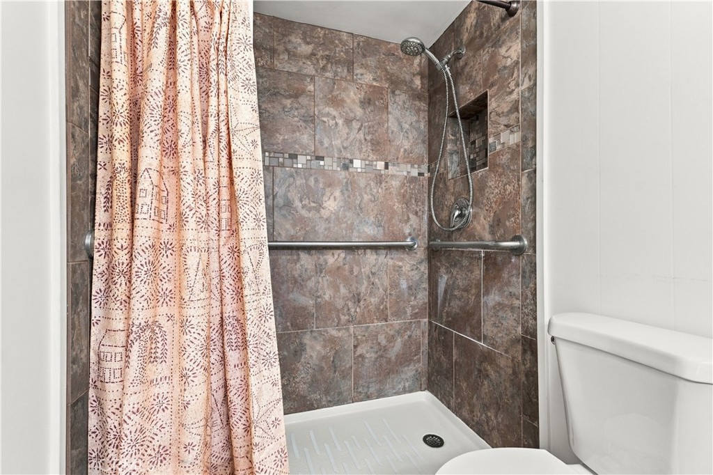 Bathroom with a tiled walk-in shower, grab bars, patterned curtain, and handheld showerhead.