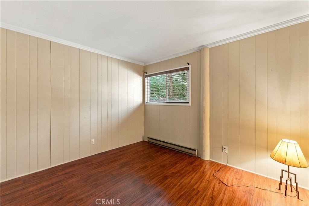 Unfurnished room with reddish wood floors, beige paneled walls, a window, and a baseboard heater.