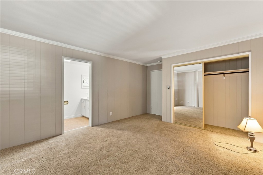 Empty bedroom with beige carpet, paneled walls, and an open closet.