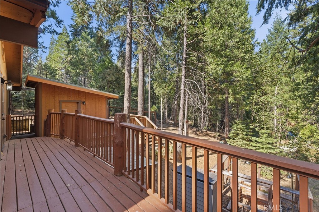 Wooden cabin deck with brown railings overlooking tall pine trees.