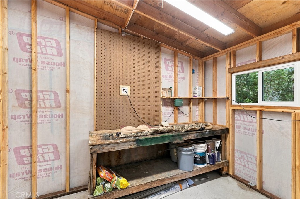 Workshop with exposed framing, a pegboard wall, and a long workbench beneath a window.