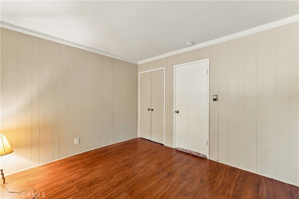 Empty bedroom with beige paneled walls, hardwood floors, and double closet doors.