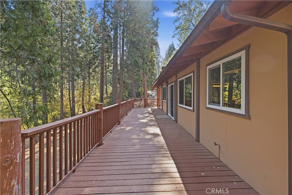 Wooden deck alongside a tan house, overlooking a wooded area of tall pine trees.