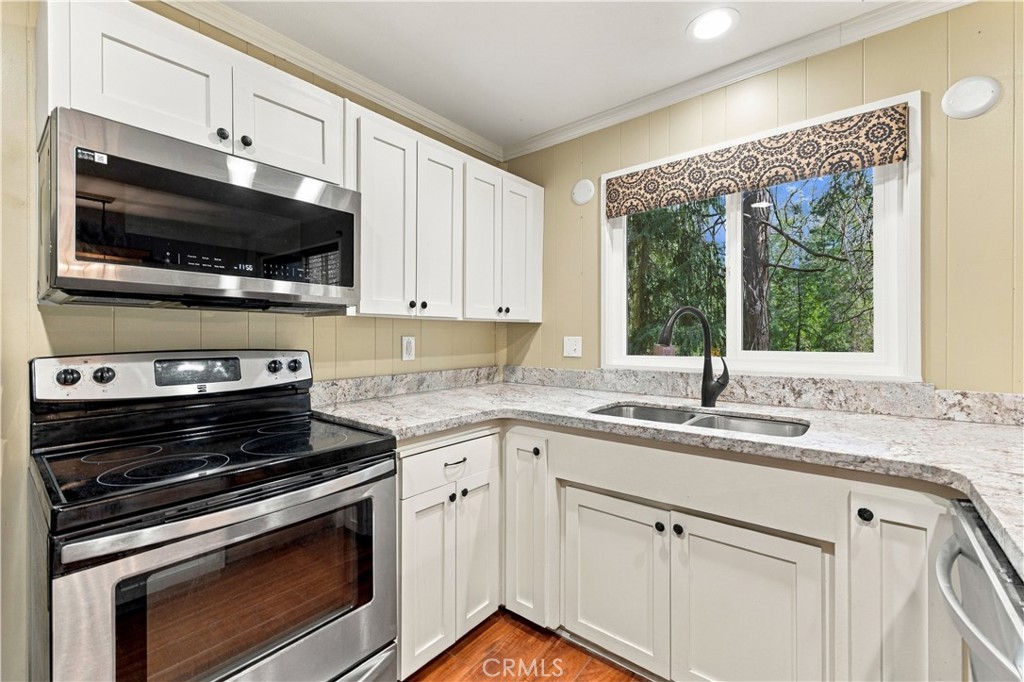 Kitchen with white cabinets, stainless steel appliances, stone counters, and a window overlooking trees.