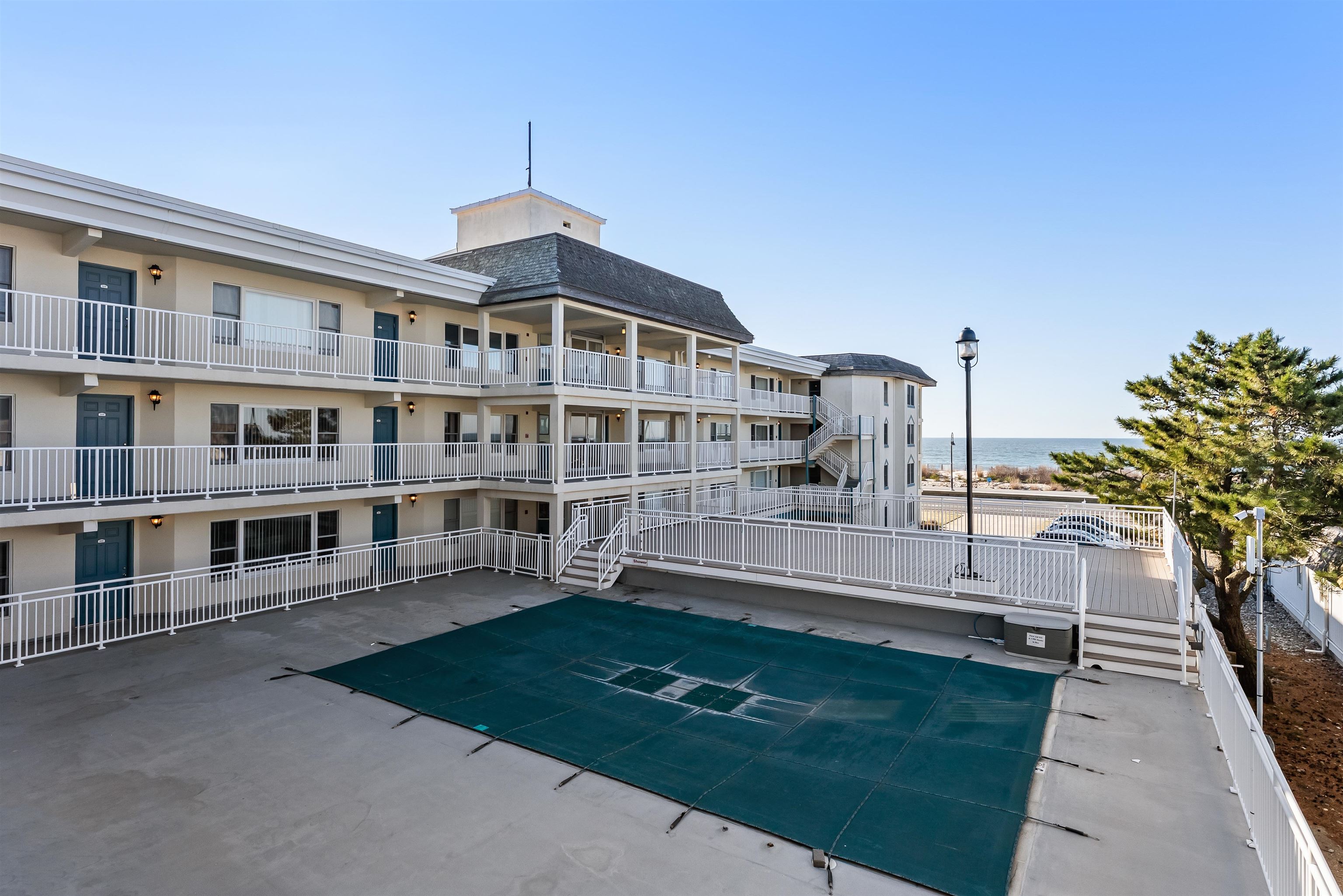 Beachfront condominium with tiered balconies, a covered pool, and ocean visible behind it.