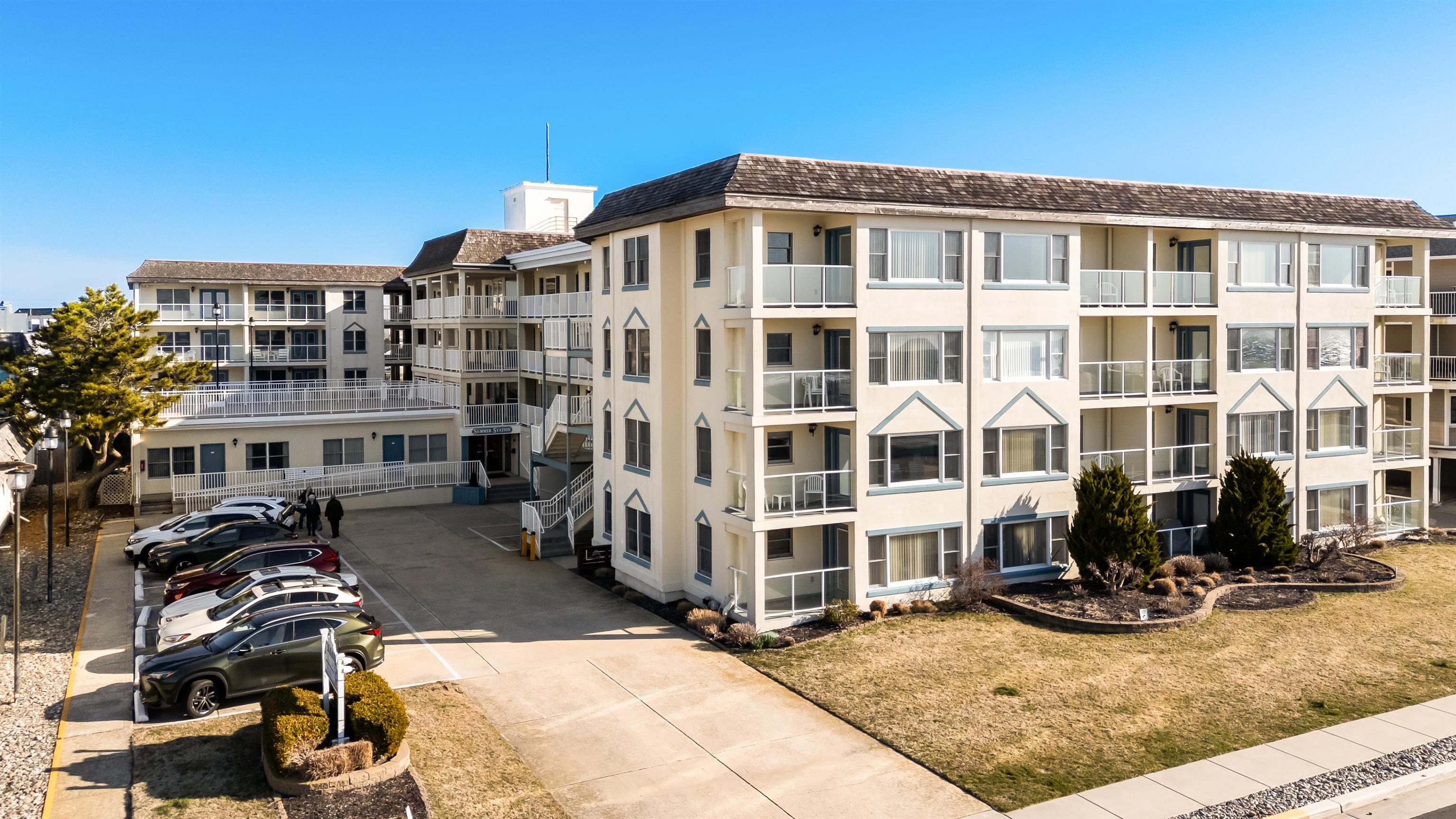 Multi-story condominium building with balconies, a parking area, and landscaped lawn.