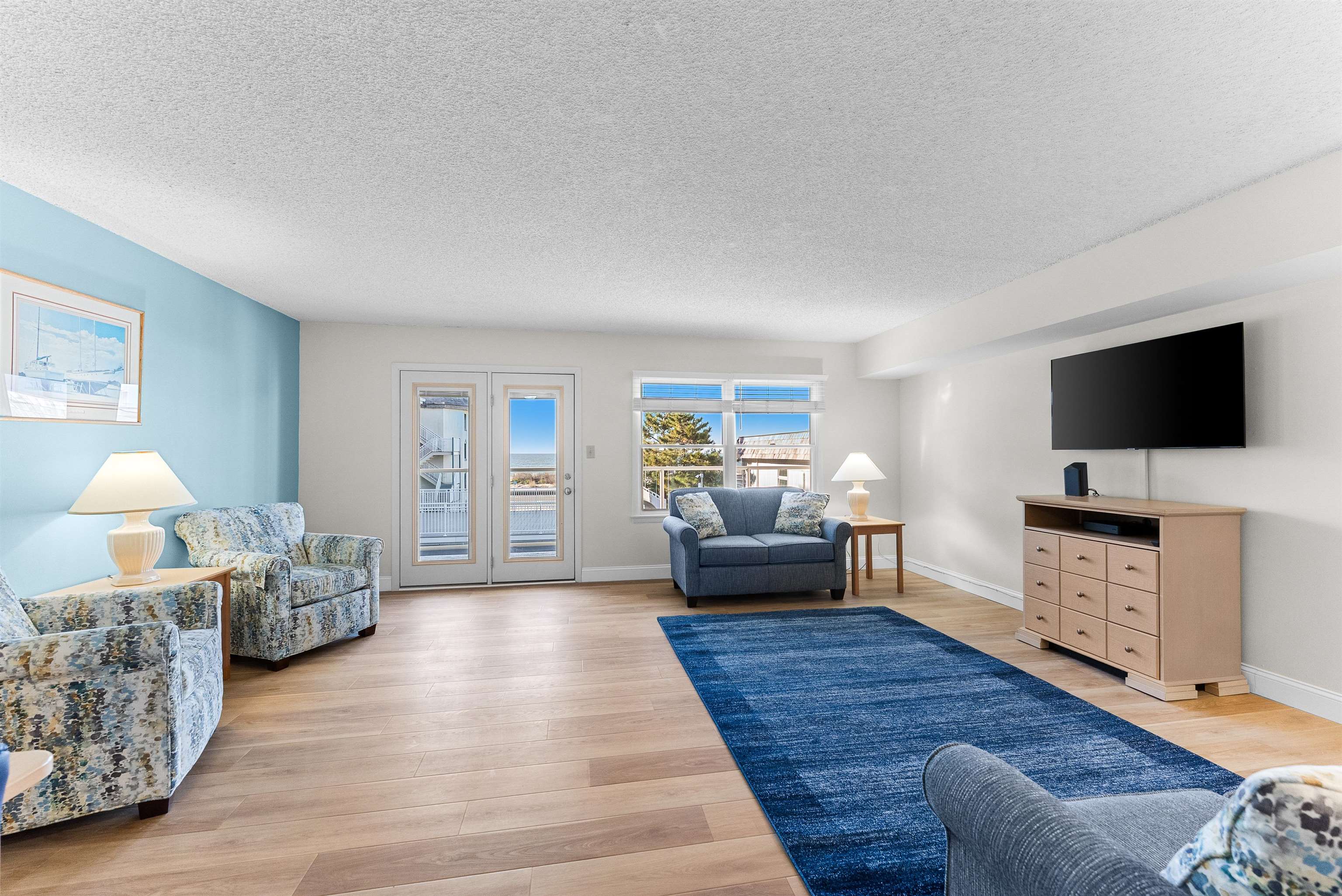 Furnished living room with blue seating, a large rug, and ocean views through glass doors.