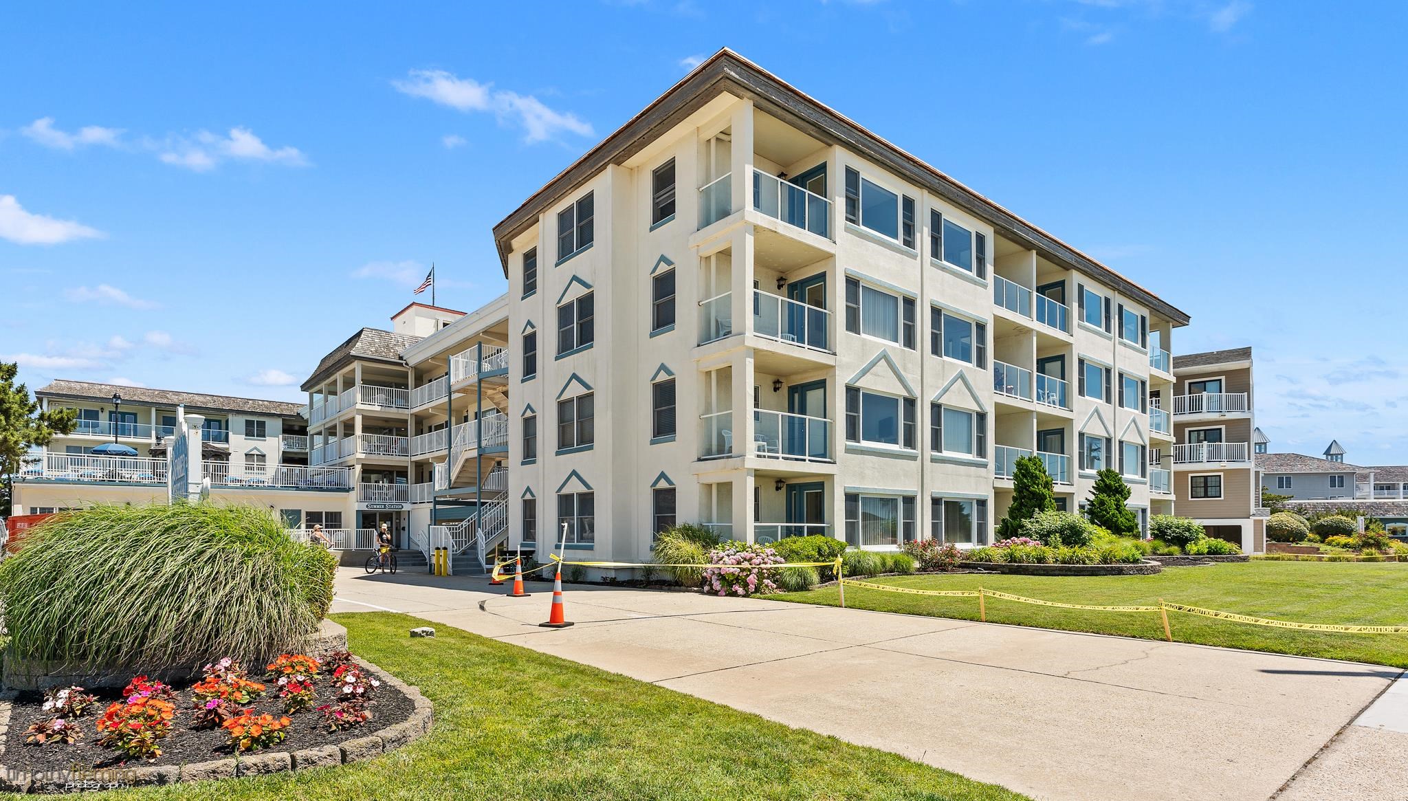 Condominium building with glass balconies, landscaped gardens, and a paved entrance walkway.
