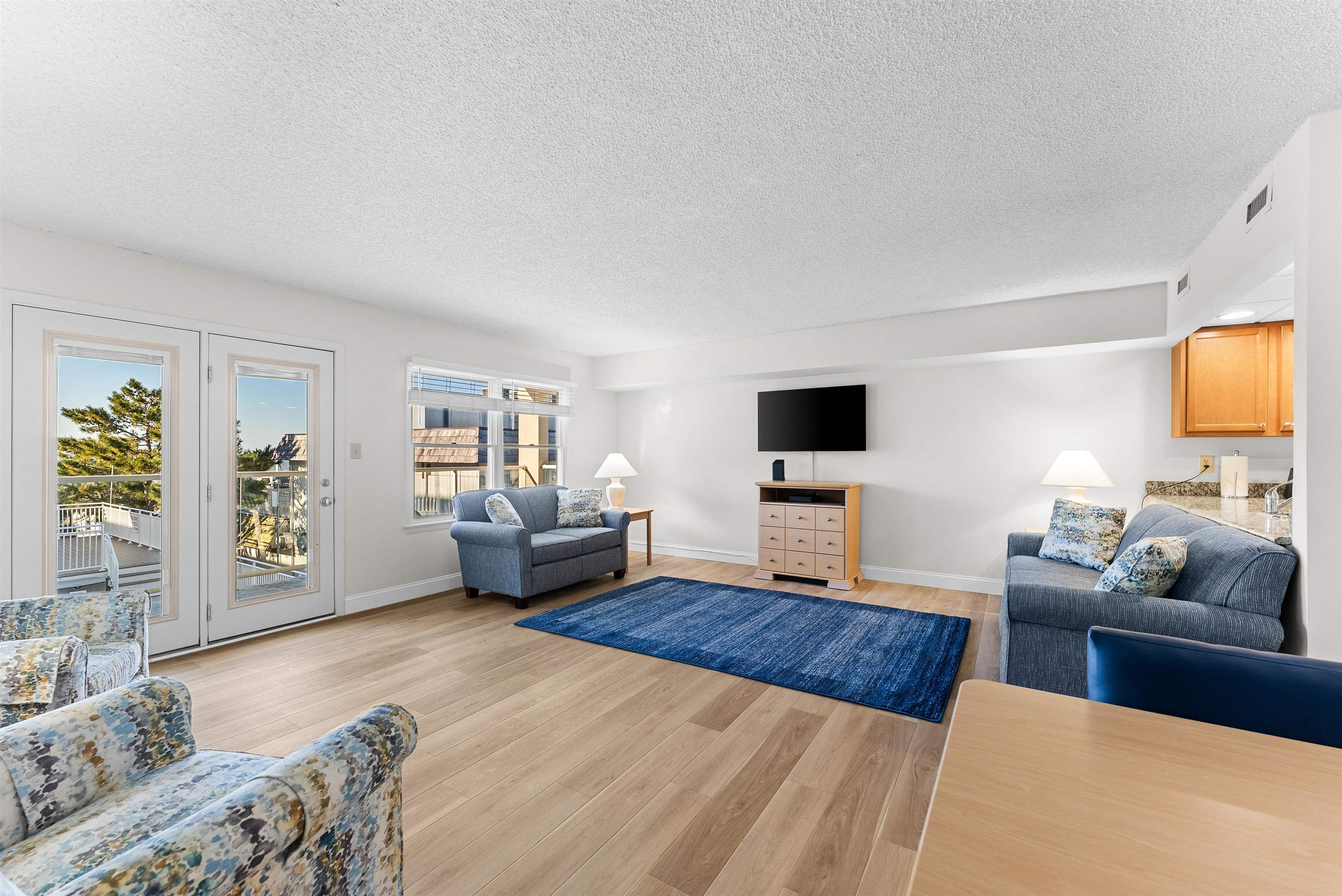Living room with blue sofas, patterned armchairs, a blue rug, and glass doors to a balcony.