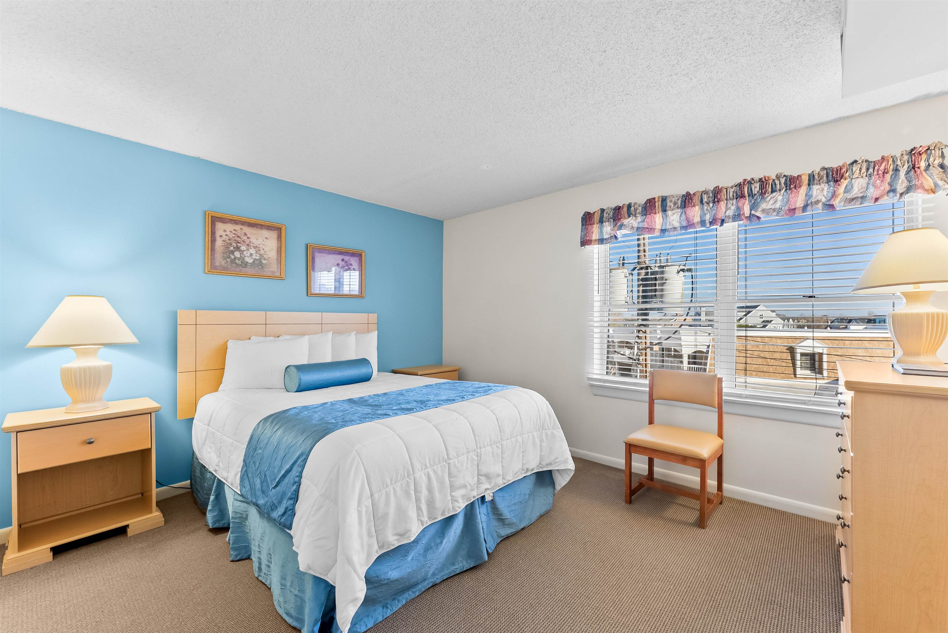 Bedroom with a blue accent wall, white-and-blue bed, and window overlooking rooftops.