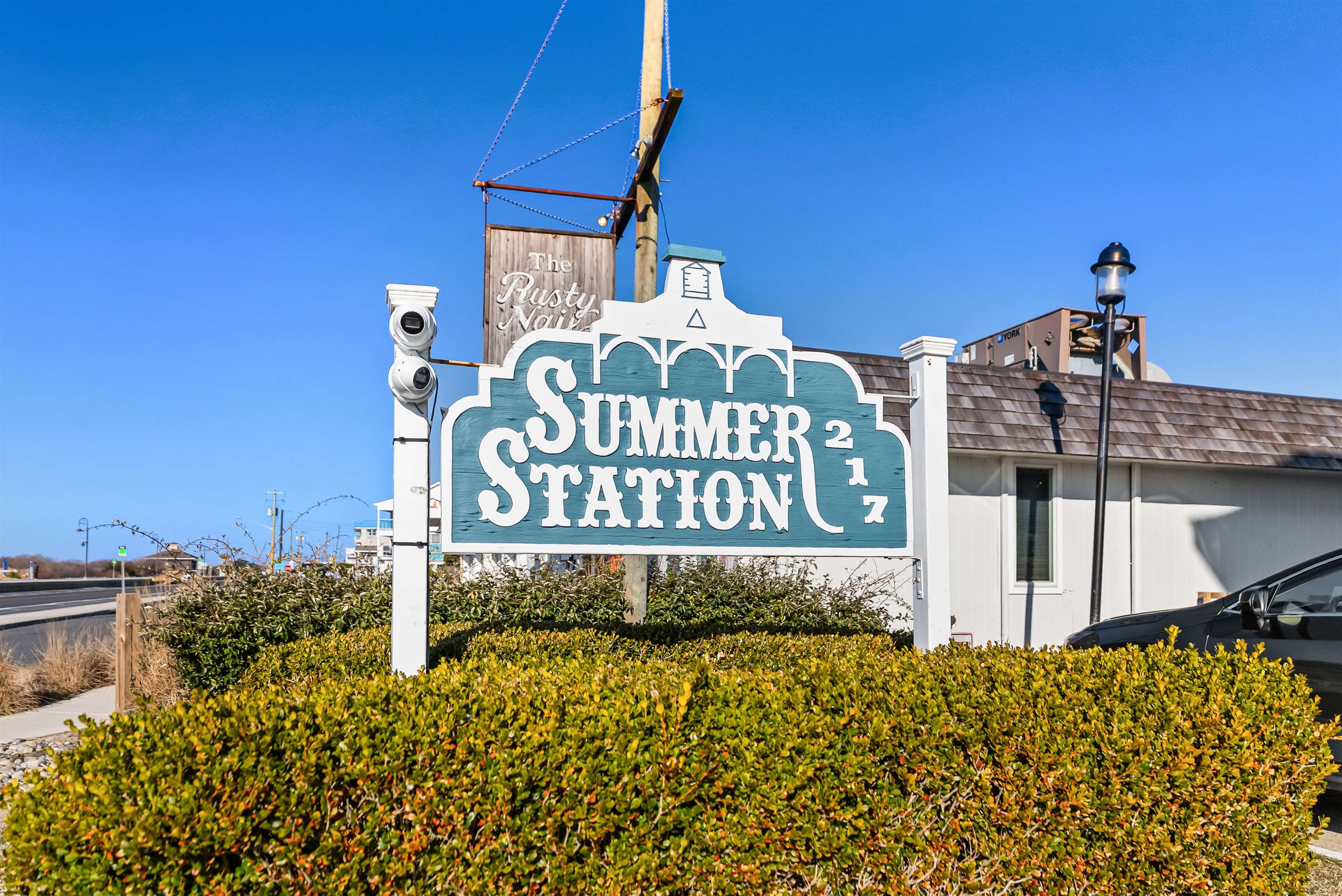 Summer Station 217 sign beside a low building and hedge.