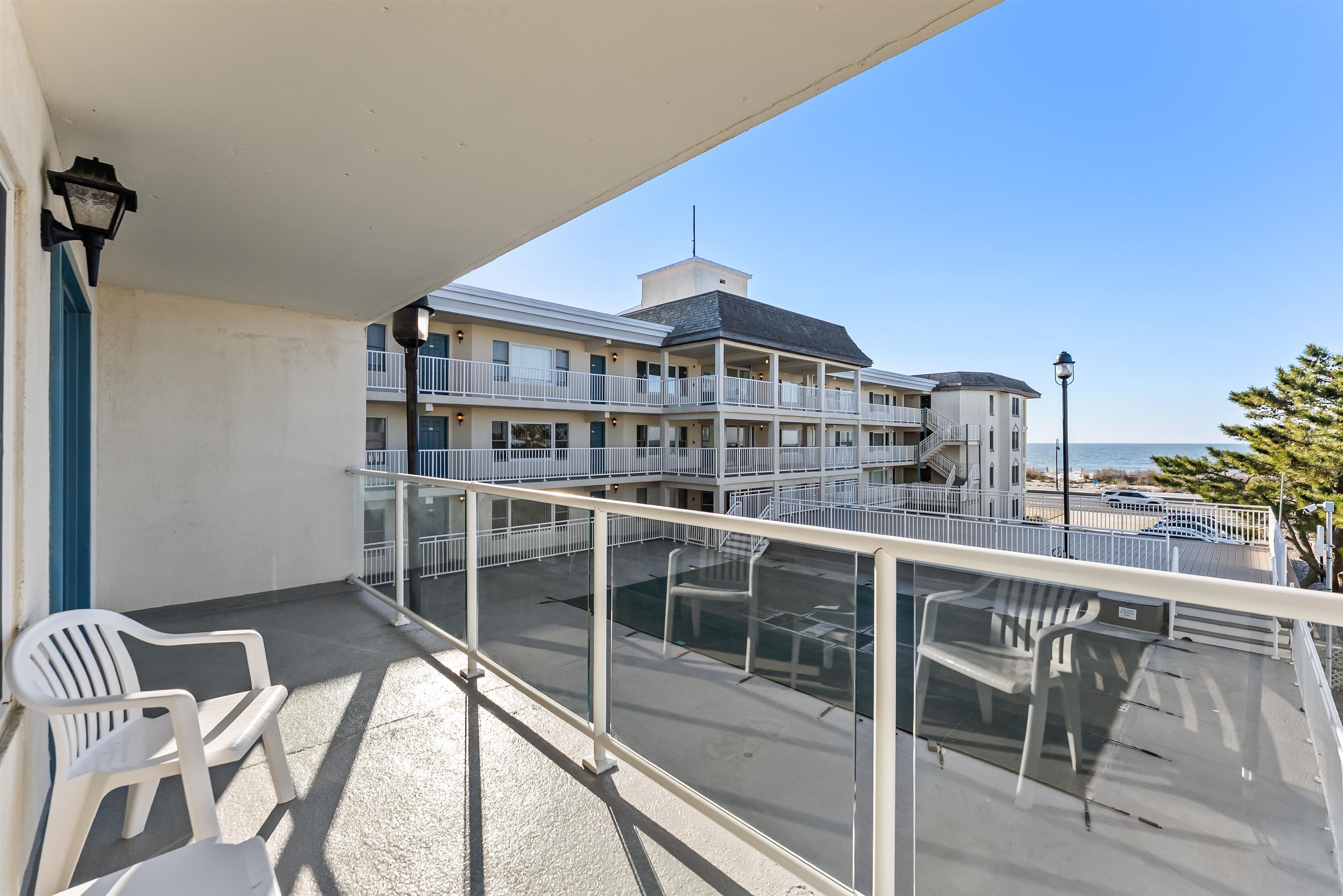Condo balcony with glass railing and chairs overlooking the ocean and neighboring building.