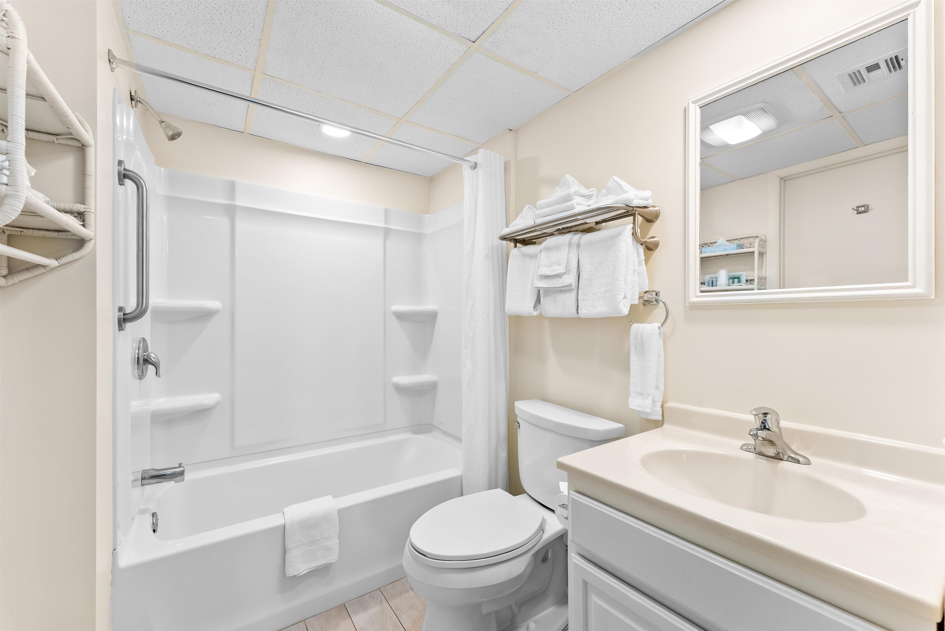 Bathroom with a white tub and shower, toilet, vanity, and towels.