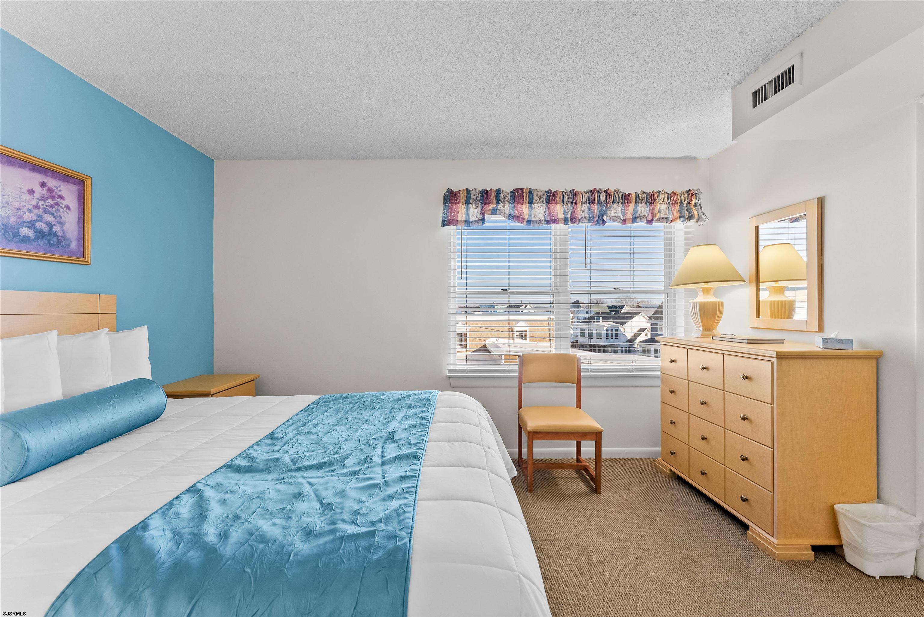 Furnished bedroom with a blue quilt, turquoise accent wall, and window overlooking nearby houses.