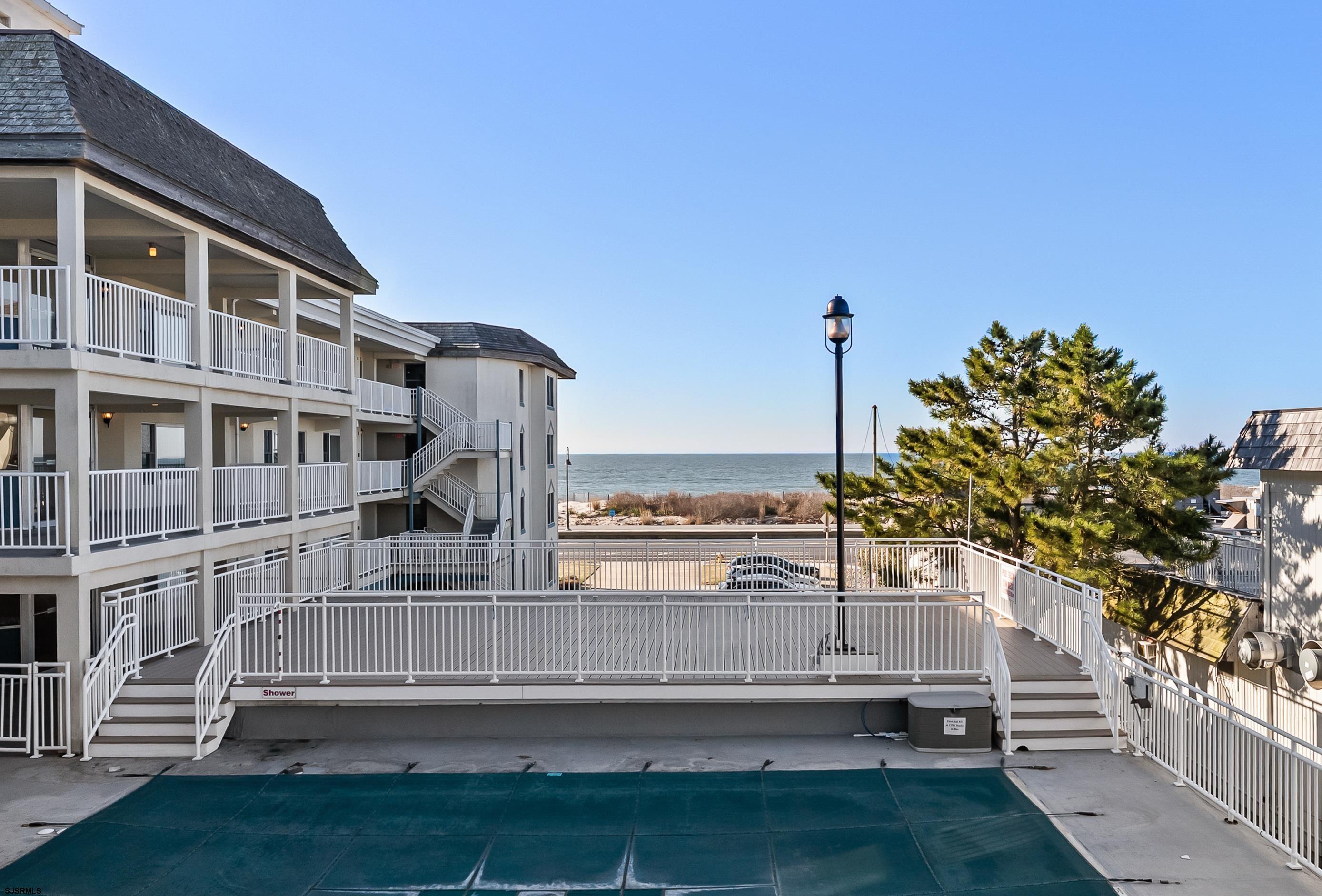 Outdoor pool beside a coastal condominium, with the ocean visible beyond the railings.
