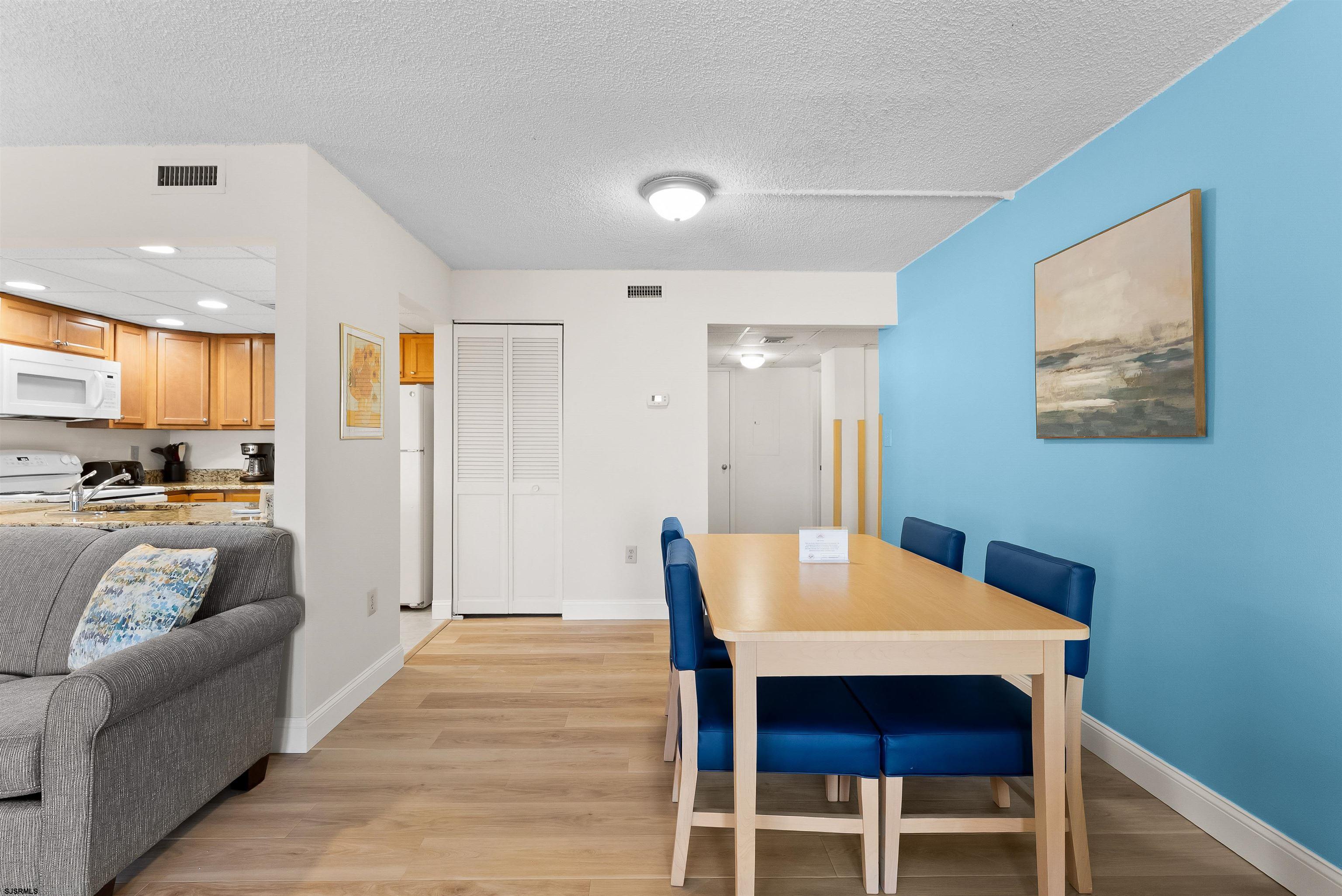 Dining area with blue chairs and accent wall, open to a kitchen and gray sofa.