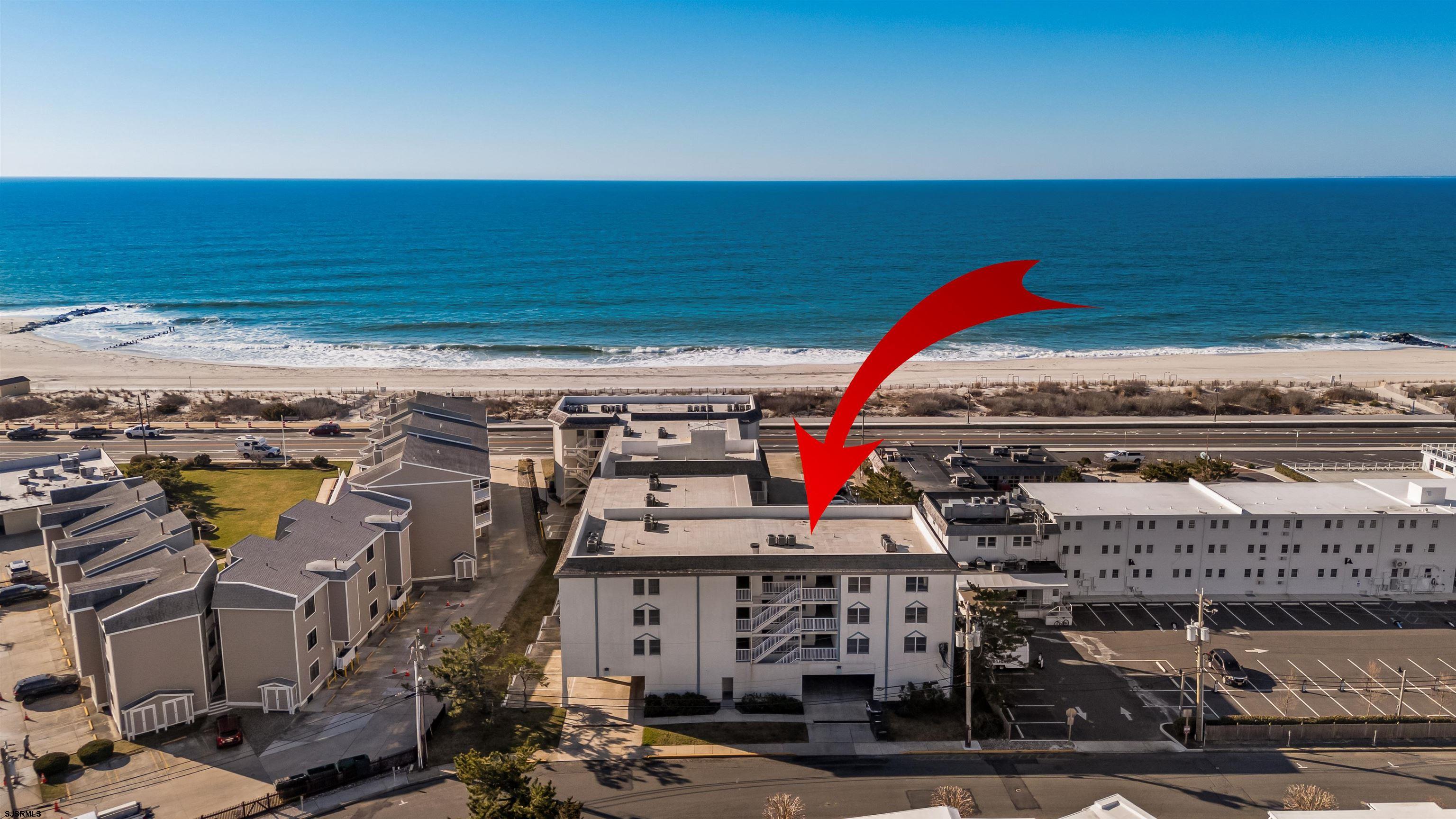 Aerial view of the condominium building marked by a red arrow, with the beach and ocean behind it.