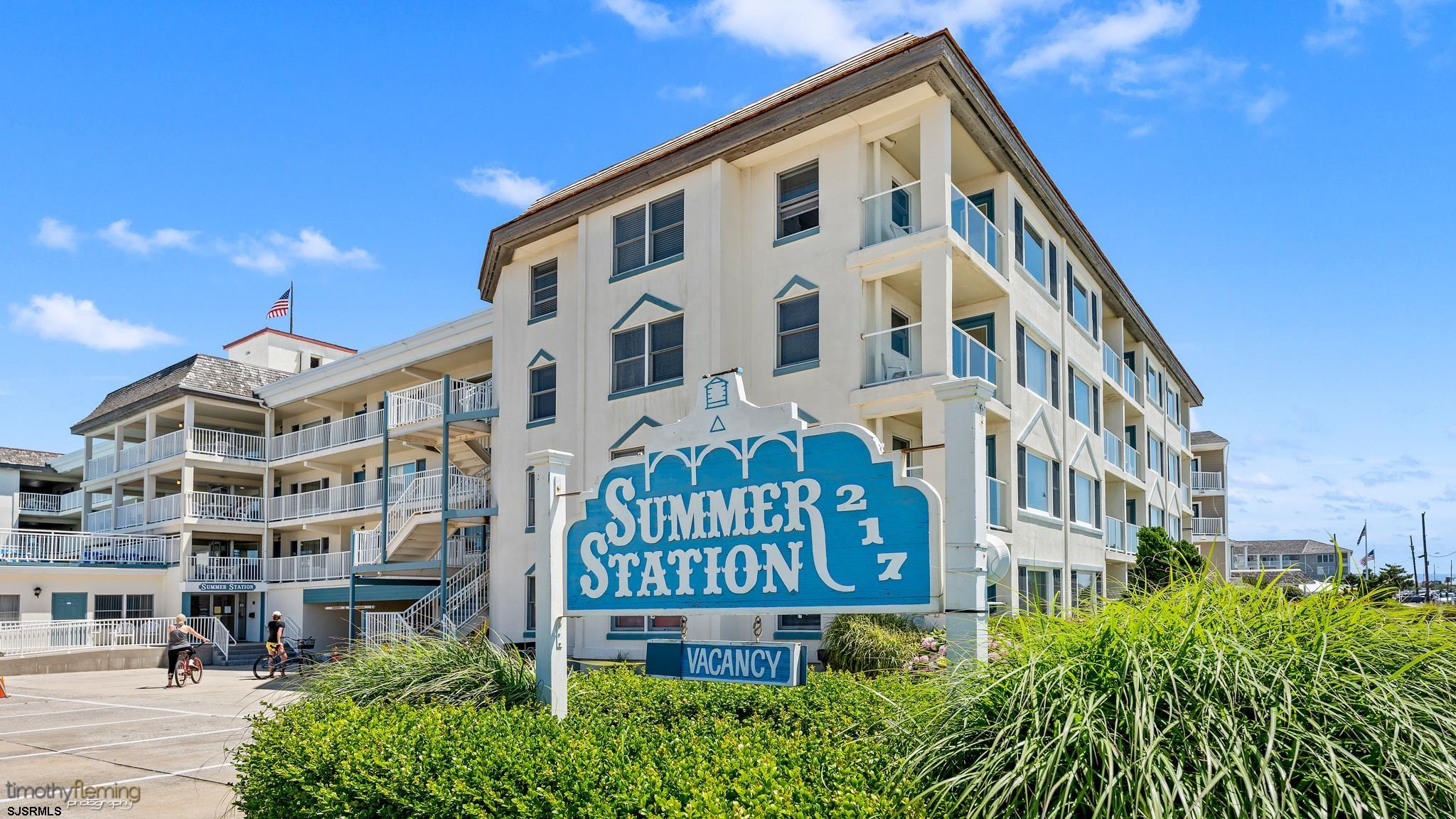 Coastal condominium with white balconies, a large Summer Station sign, and dune grasses.