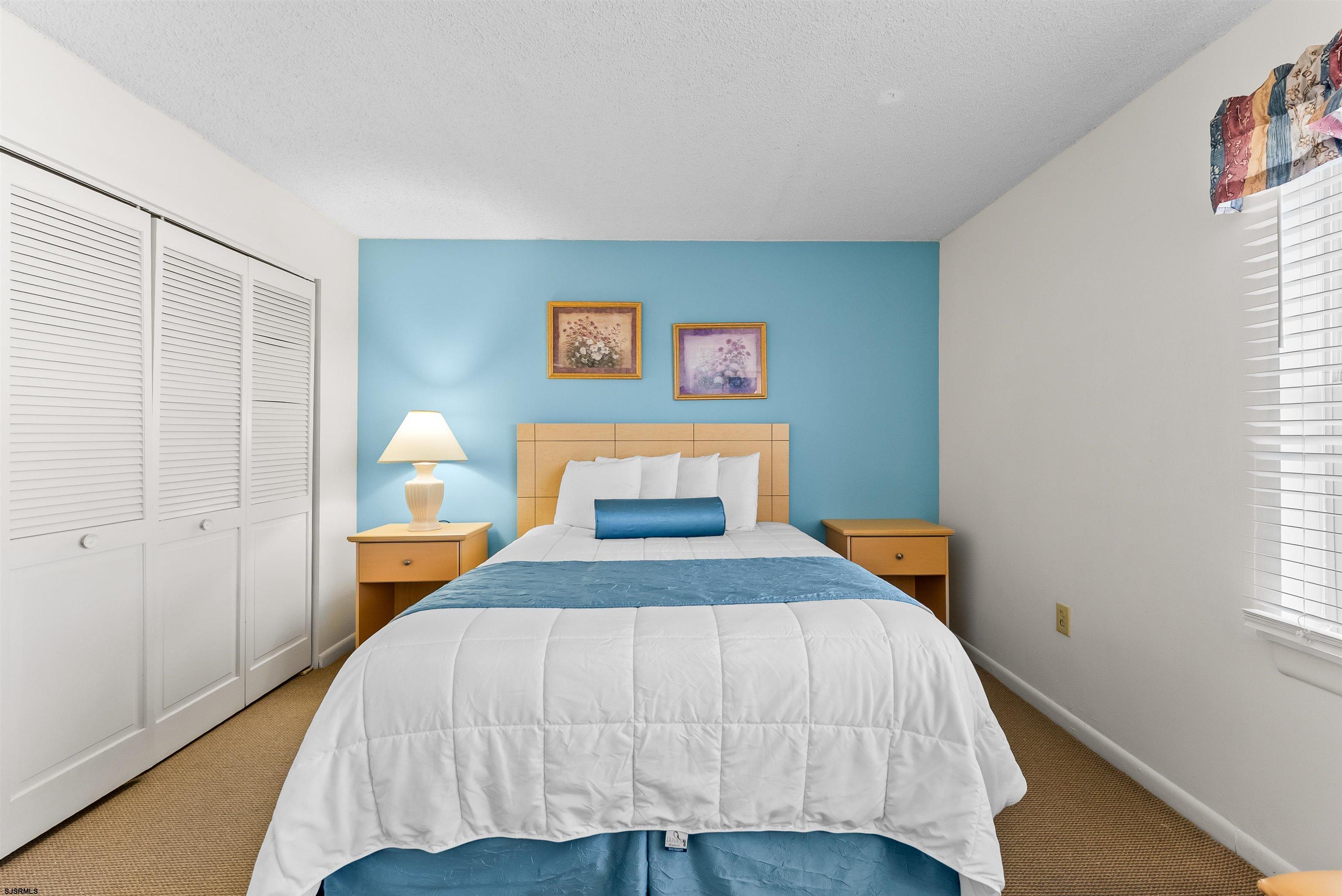 Bedroom with a white bed, blue accents, turquoise wall, and louvered closet doors.