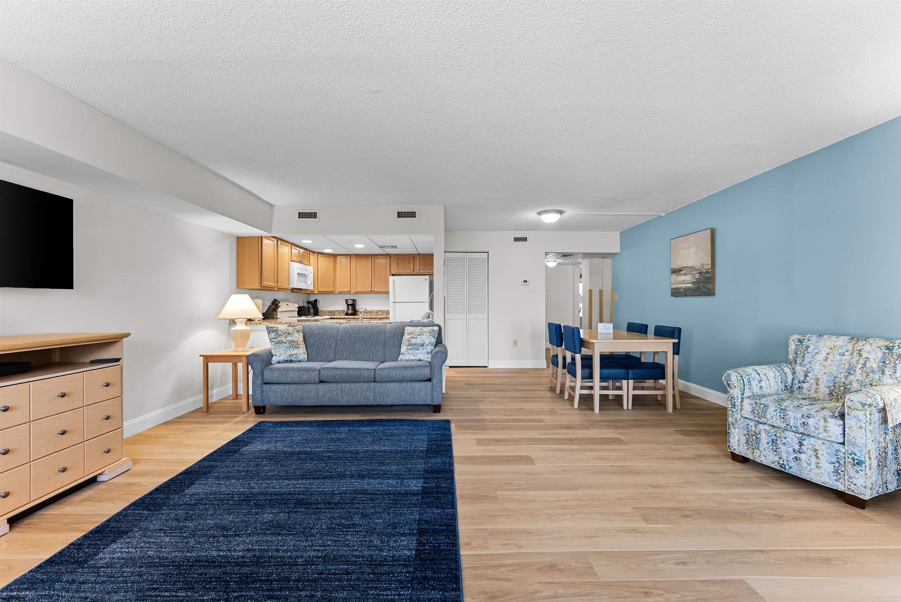 Open-plan living room with a navy rug, blue sofa, dining area, and kitchen.