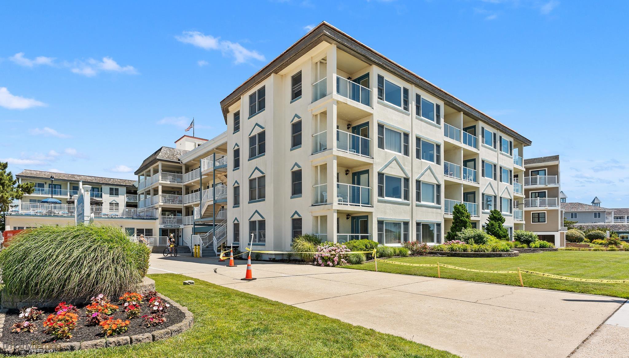 Cream-colored condominium building with glass-railed balconies and landscaped grounds.