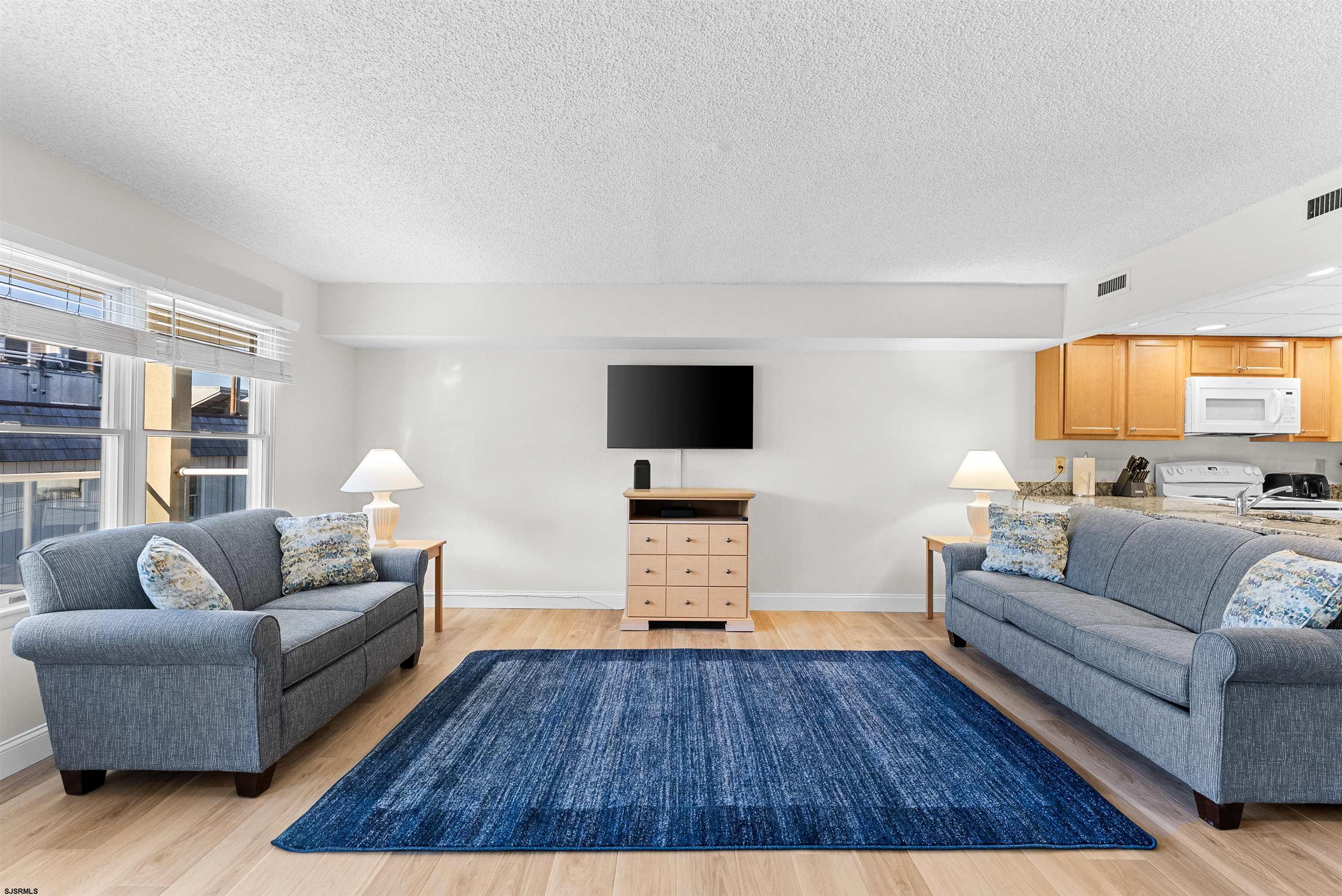 Furnished living room with two gray sofas, a large blue rug, and an open kitchen.