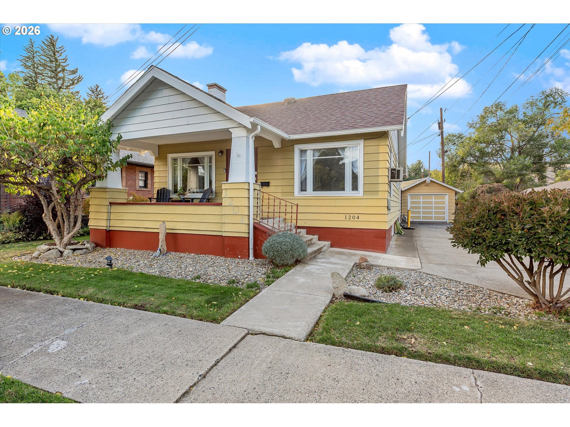 Yellow-sided house with a covered porch, red foundation, and detached garage.