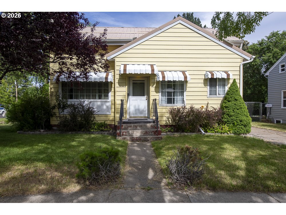 Yellow house with striped awnings, front steps, and a walkway through the lawn.