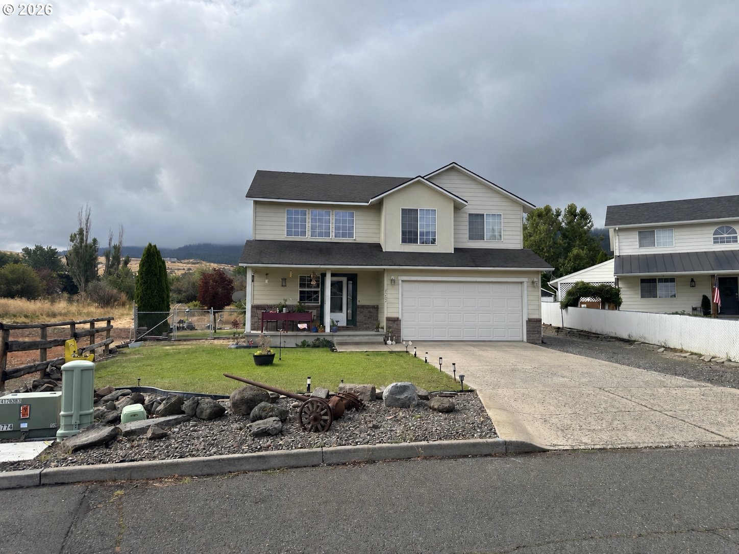 Two-story beige house with a double garage, covered porch, and small lawn.