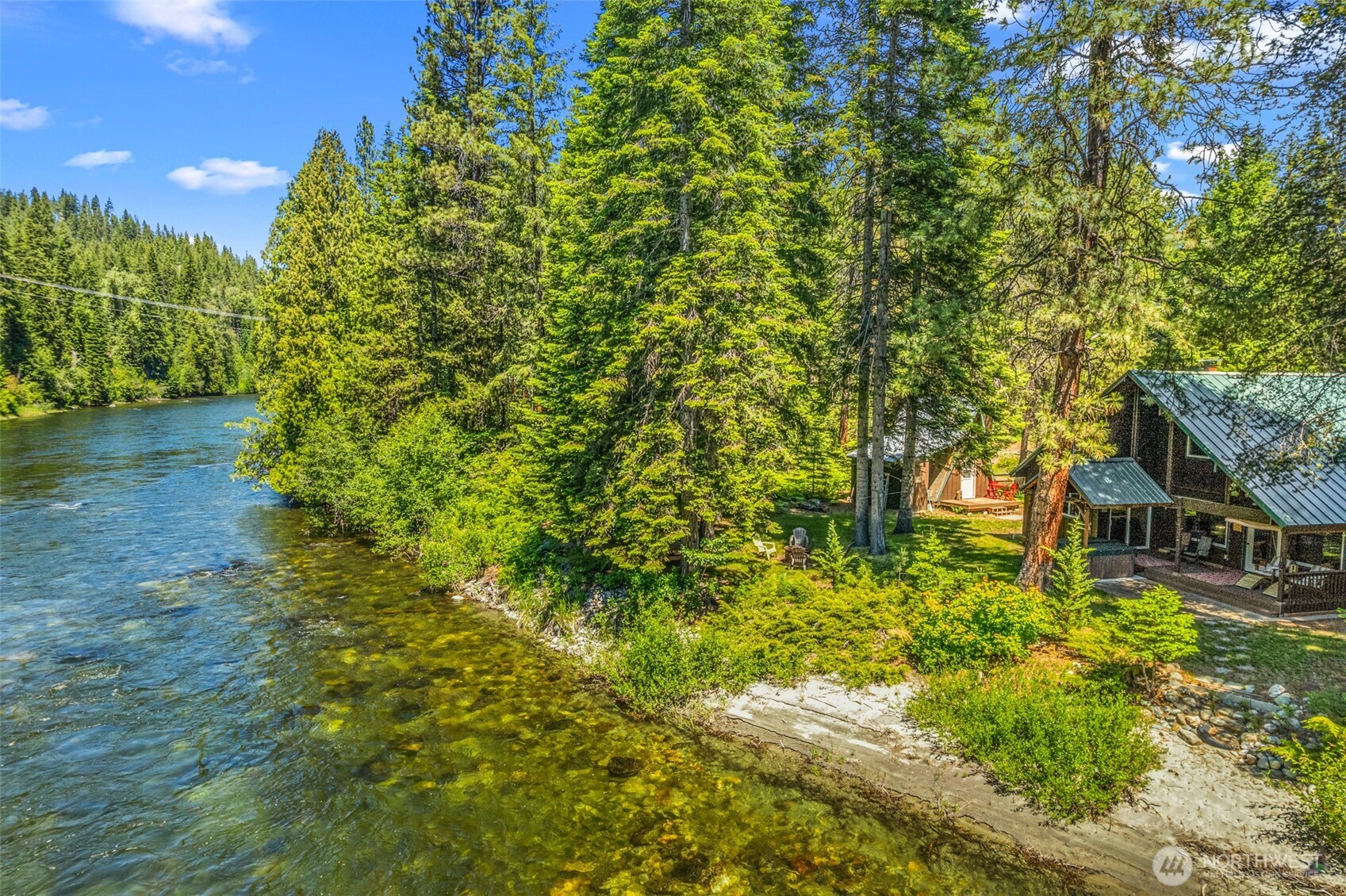 Cabins and a lodge sit among evergreens beside a clear river.
