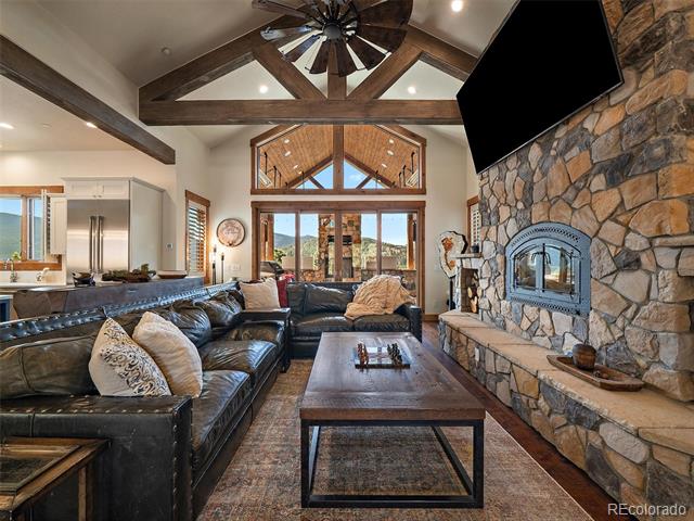 Vaulted living room with exposed beams, a stone fireplace, leather sectional, and open kitchen.