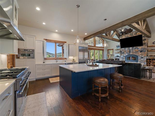 Kitchen with a dark blue island, exposed timber beams, and a stone fireplace beside the living area.