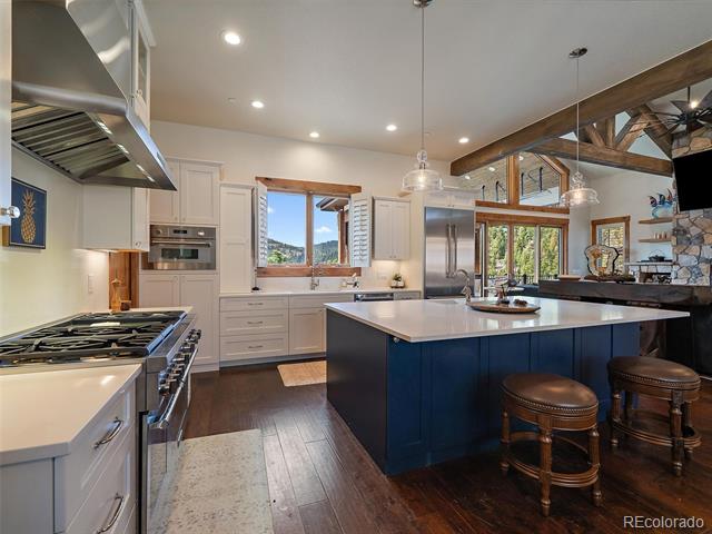 Kitchen with a navy island, stainless appliances, exposed timber beams, and windows overlooking trees.