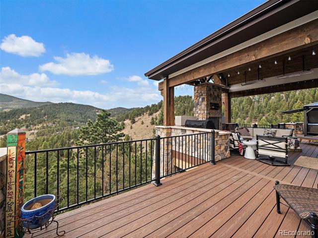 Covered mountain-view deck with wood flooring, black railing, and outdoor seating.